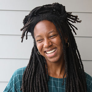 Close-up author photograph of Angela Tharpe smiling and looking to the left. She has on a plaid dark teal shirt and hoop earrings.